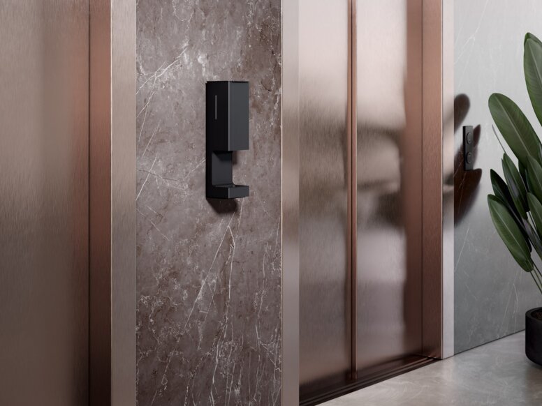 A touch-free disinfectant dispenser is installed on the wall between two elevator doors
